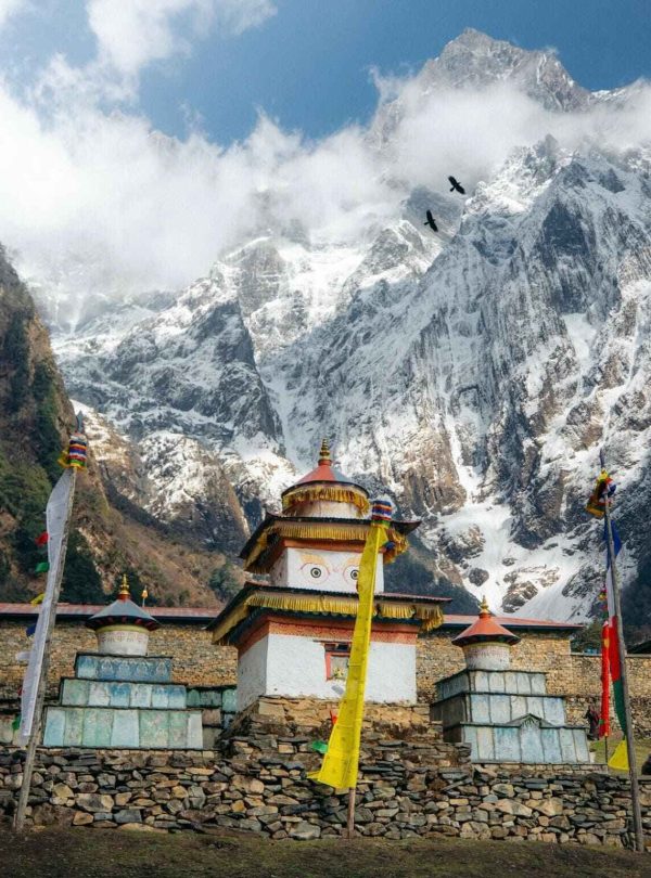 Buddhist stupa with prayer flags and snowy mountains on the Manaslu Circuit Trek in Nepal.