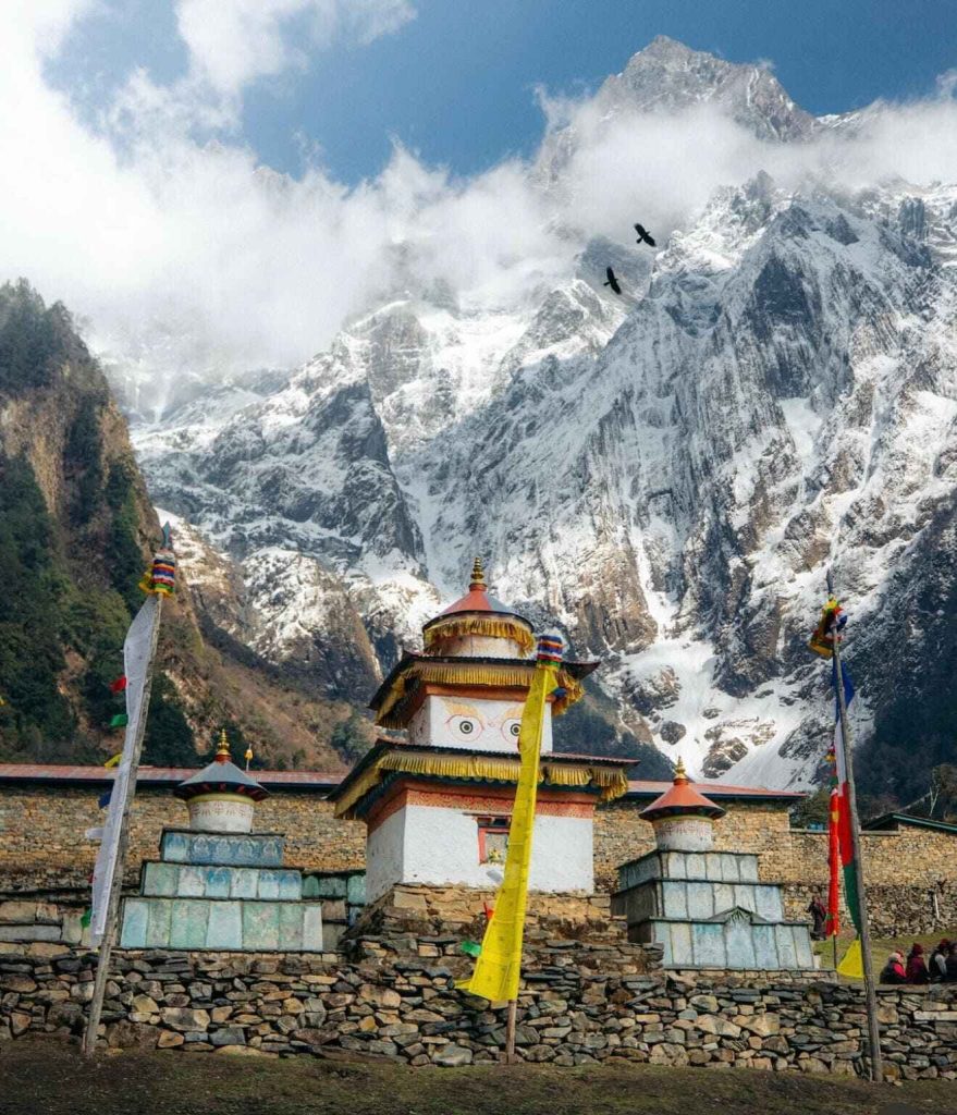 Buddhist stupa with prayer flags and snowy mountains on the Manaslu Circuit Trek in Nepal.