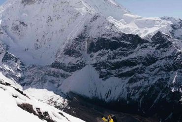 Trekker climbing snowy slopes with Manaslu mountain towering above.
