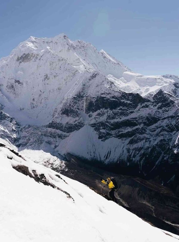 Trekker climbing snowy slopes with Manaslu mountain towering above.