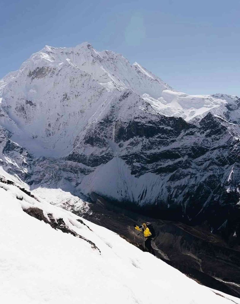 Trekker climbing snowy slopes with Manaslu mountain towering above.