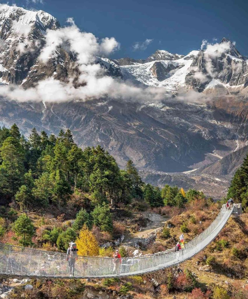 Suspension bridge on the Manaslu Circuit Trek with snow-capped mountains in the background.