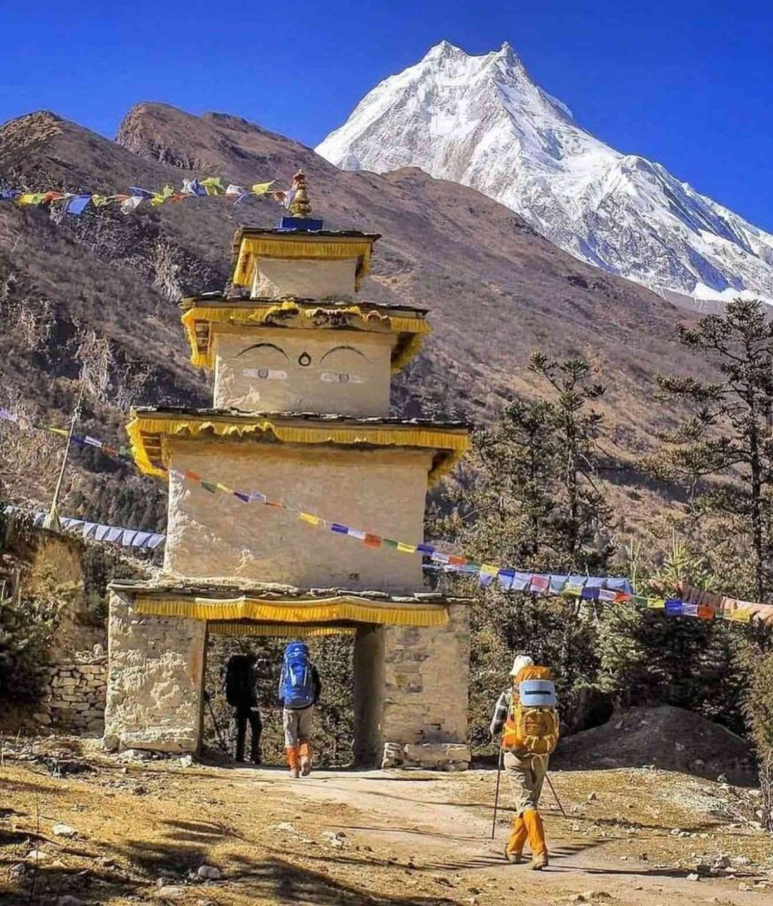 Trekkers walking through a traditional Buddhist gate with Mount Manaslu in the background.