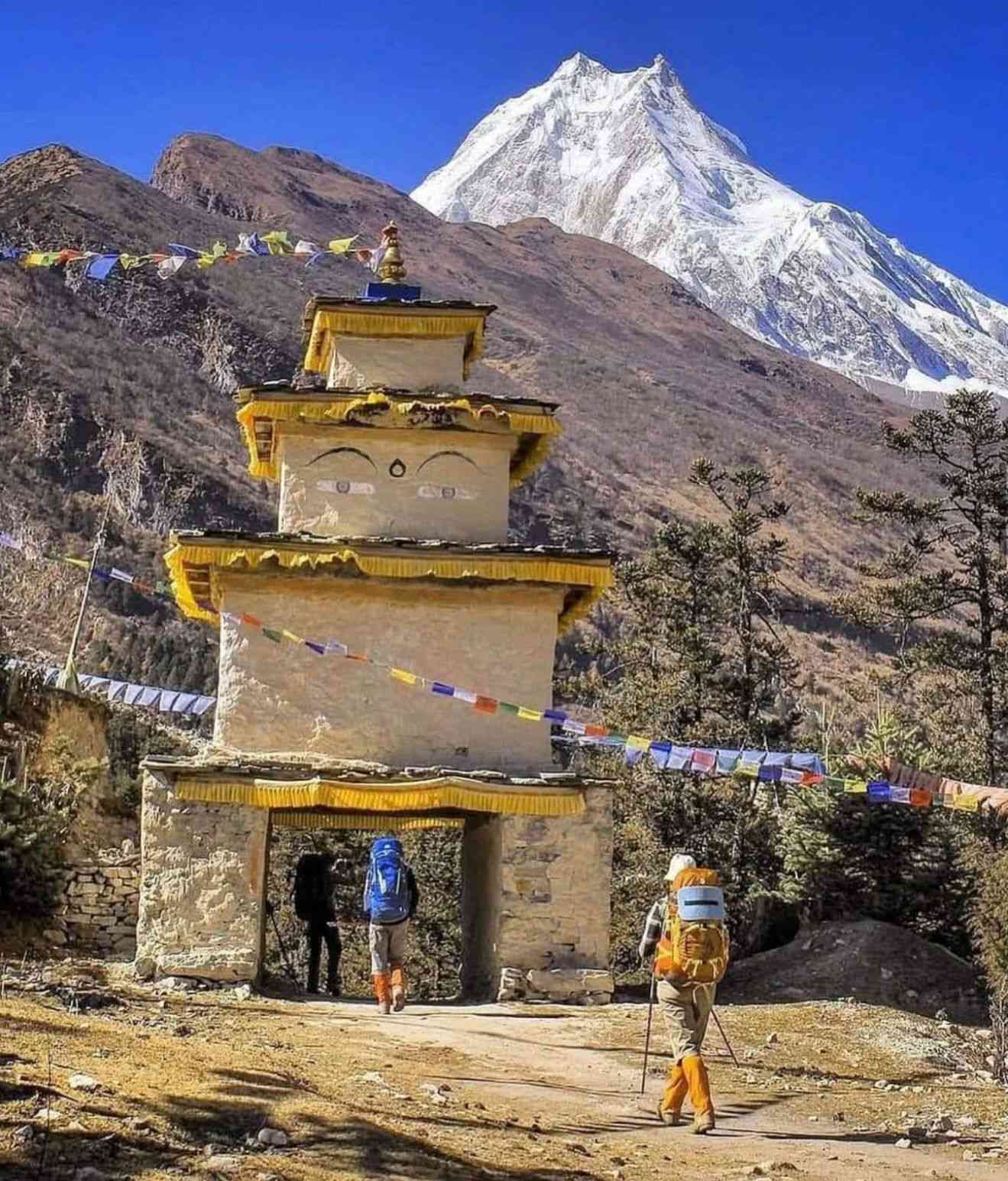 Trekkers walking through a traditional Buddhist gate with Mount Manaslu in the background.