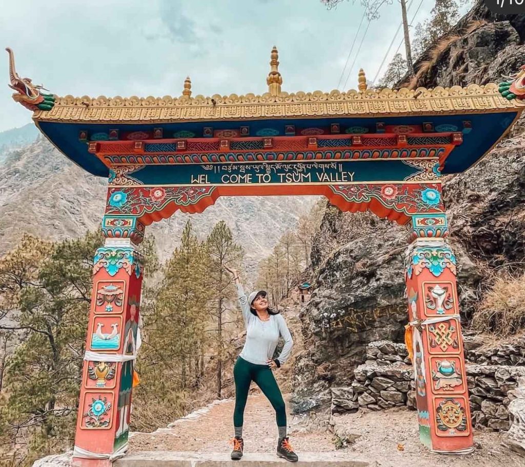 Trekker smiling with forested hills and snow-capped mountains in the Manaslu region.