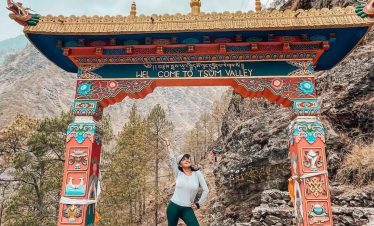Trekker smiling with forested hills and snow-capped mountains in the Manaslu region.