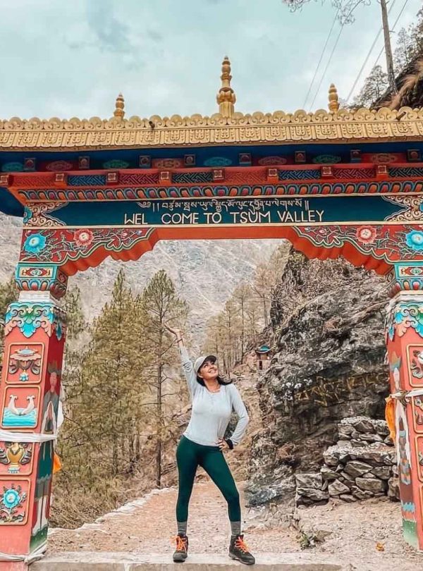 Trekker smiling with forested hills and snow-capped mountains in the Manaslu region.