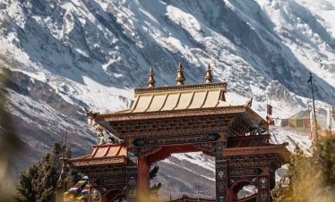 Ornate Buddhist monastery gate in Tsum Valley with towering snow-capped peaks.