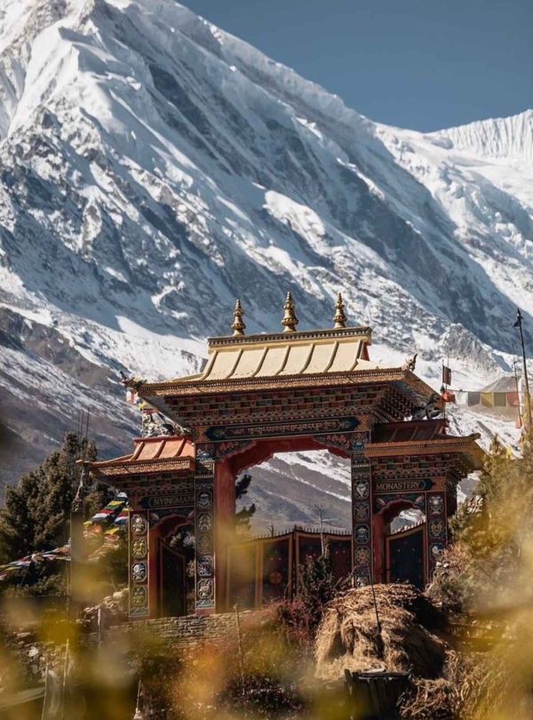 Ornate Buddhist monastery gate in Tsum Valley with towering snow-capped peaks.