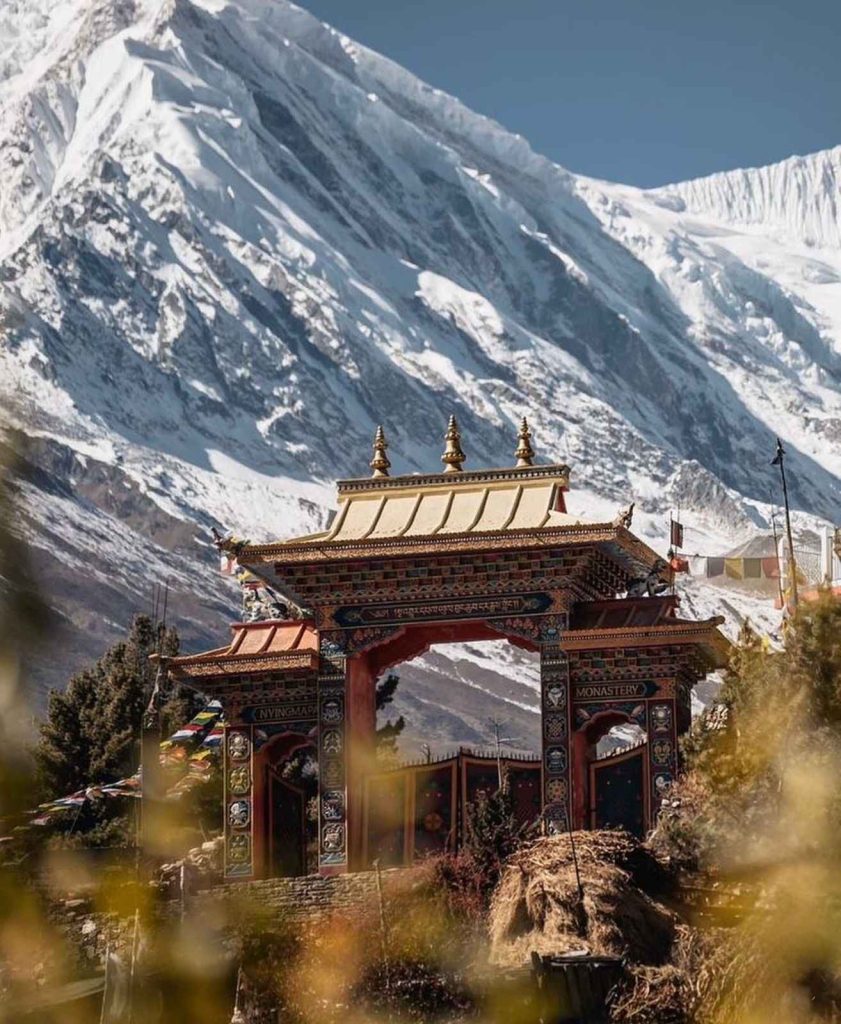 Ornate Buddhist monastery gate in Tsum Valley with towering snow-capped peaks.