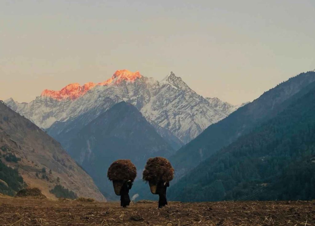 Local women carrying baskets in Tsum Valley with glowing Himalayan peaks at sunset.