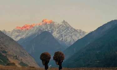 Local women carrying baskets in Tsum Valley with glowing Himalayan peaks at sunset.
