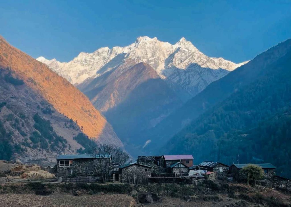 Traditional stone houses in Tsum Valley with snow-covered mountains glowing at sunrise.
