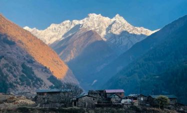 Traditional stone houses in Tsum Valley with snow-covered mountains glowing at sunrise.
