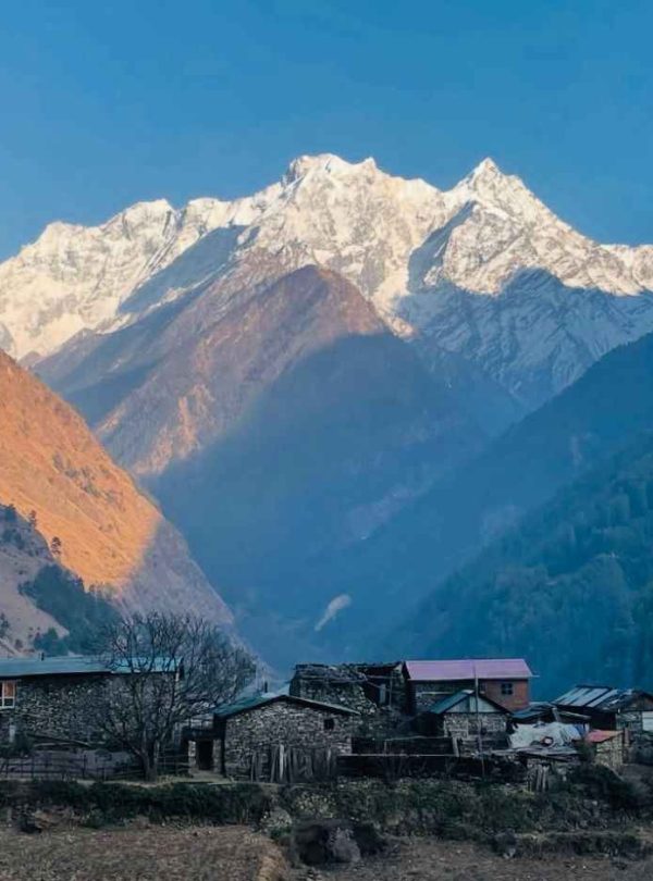 Traditional stone houses in Tsum Valley with snow-covered mountains glowing at sunrise.