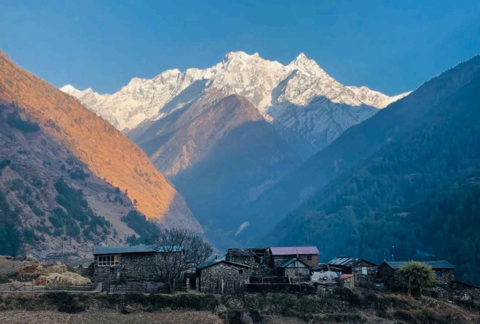 Traditional stone houses in Tsum Valley with snow-covered mountains glowing at sunrise.