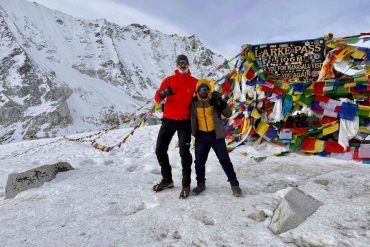 Trekkers standing at Larke Pass 5106m with prayer flags on Manaslu Circuit trek Nepal in snowy conditions
