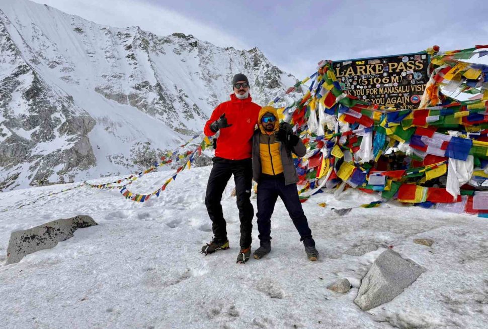 Trekkers standing at Larke Pass 5106m with prayer flags on Manaslu Circuit trek Nepal in snowy conditions