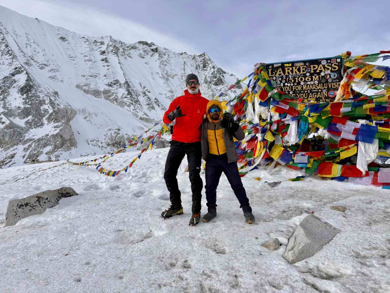 Trekkers standing at Larke Pass 5106m with prayer flags on Manaslu Circuit trek Nepal in snowy conditions